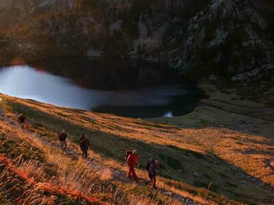 Escursionisti in cammino all'alba: alle loro spalle il rifugio Dante Livio Bianco e il Lago inferiore della Sella | G. Bernardi - Archivio APAM
